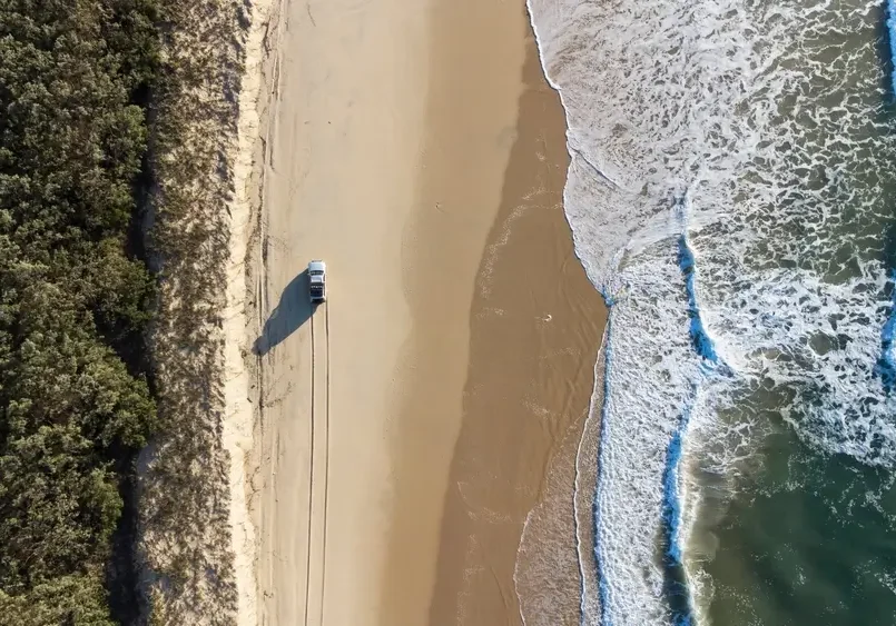 Aerial shot captures a serene beach 4WD vehicle driving along the coast